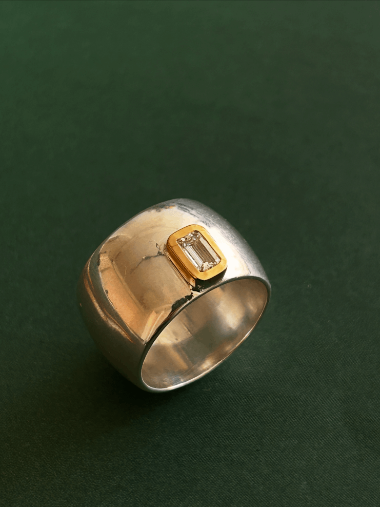 Silver ring with a square diamond set in gold, on a dark green background